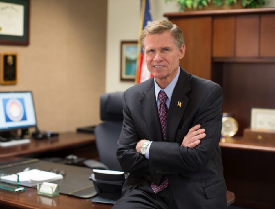 Greg Totten sitting on desk with arms crossed
