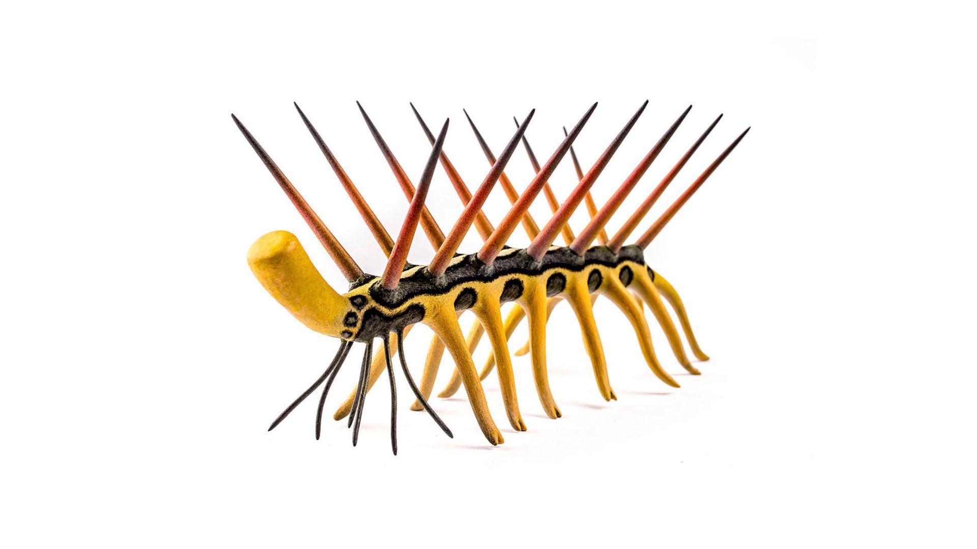 A vibrant yellow and black sculpture of a spiky marine animal with elongated body and numerous sharp, red and black spines protruding upwards