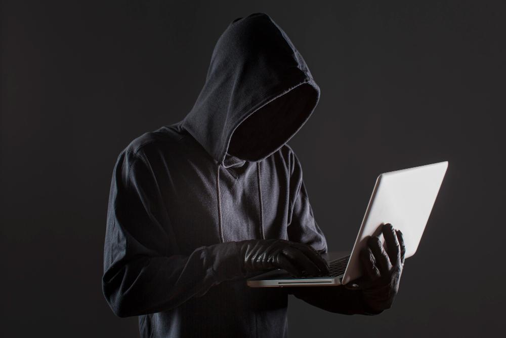 A man dressed in all black is pictured looking at a laptop screen