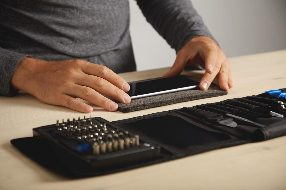 A man is pictured seated at his desk as he prepares to fix a smartphone