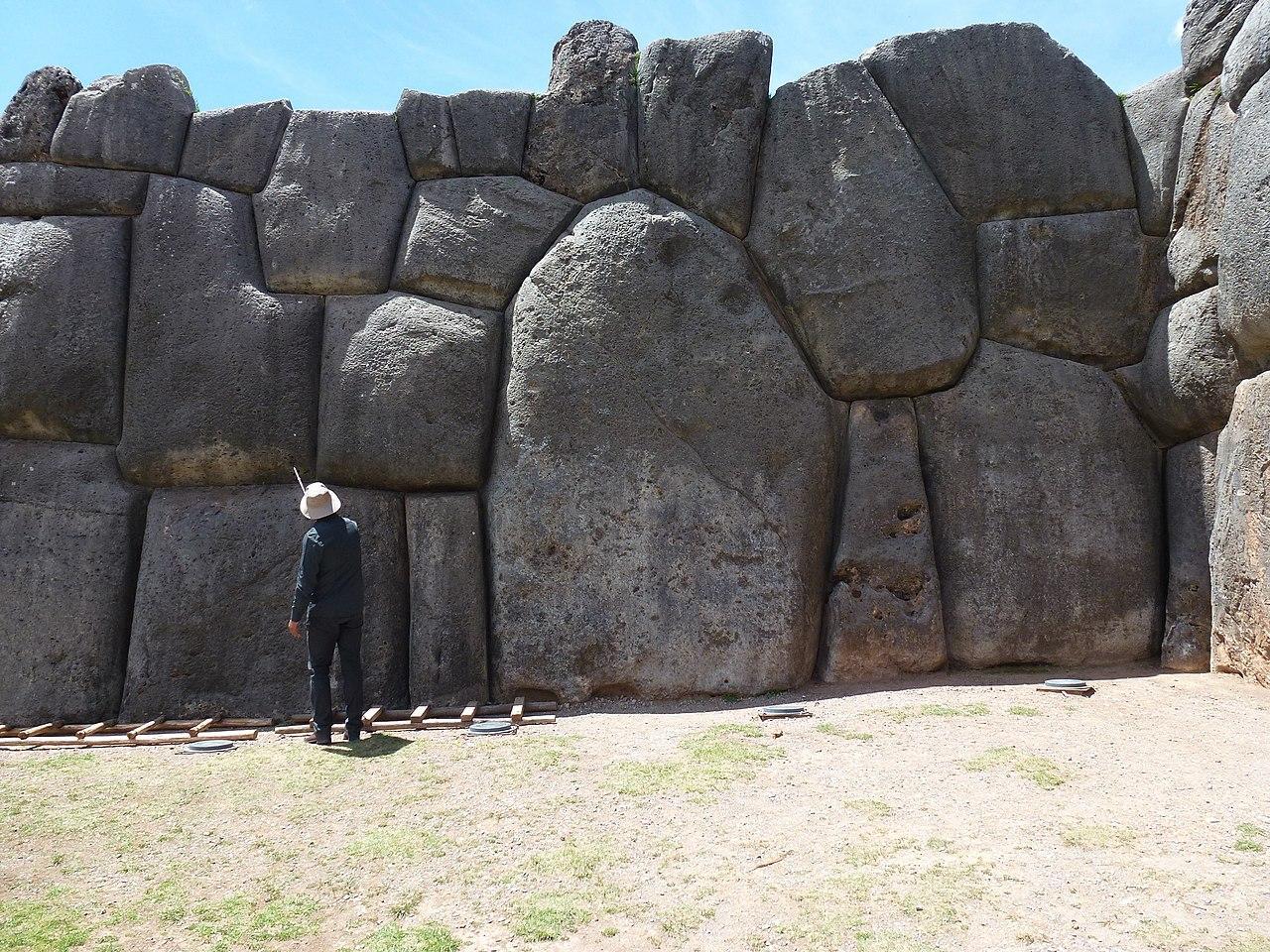 A photograph of a man standing beside the enormous blocks at Sacsayhuaman