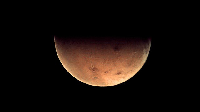 A view of Mars with dark shadows against the black backdrop of space