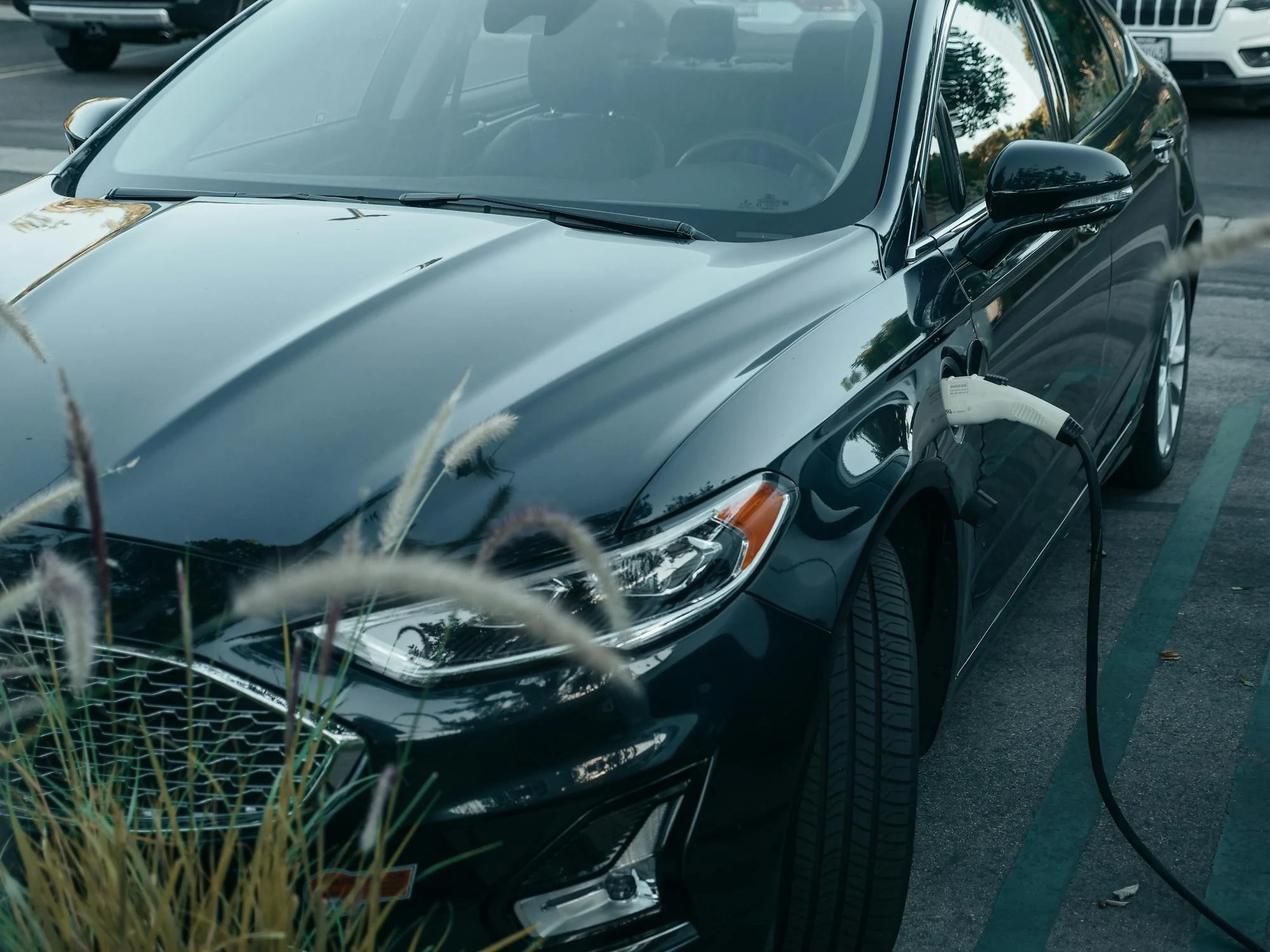 A black EV charging by a bush