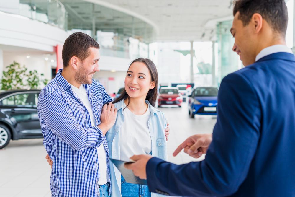 A couple pictured speaking with a salesman as they shop for a new car