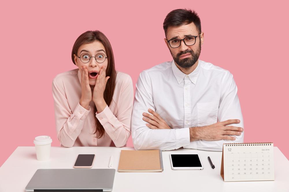 Two people pictured with shocked faces seated at their desk