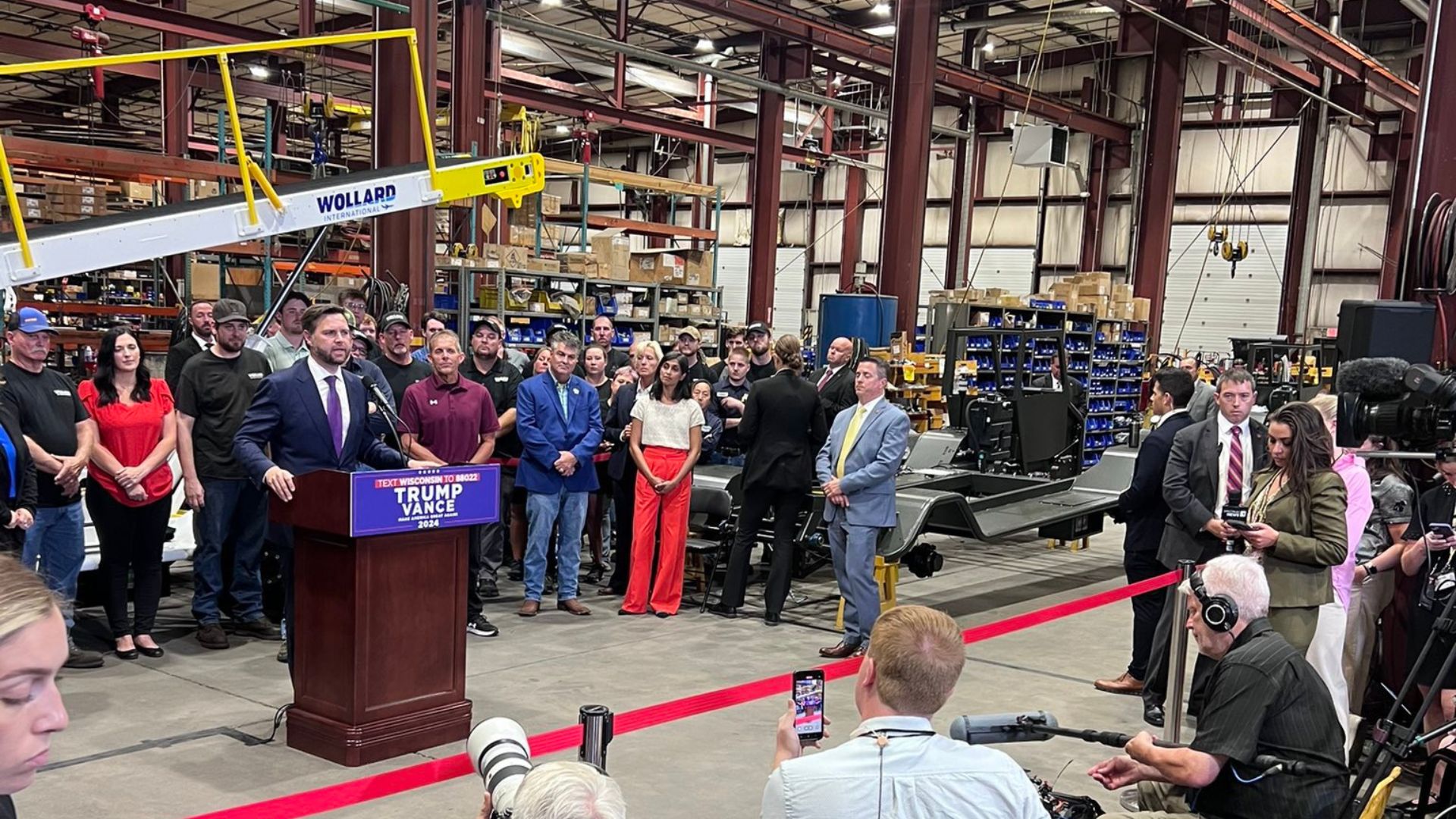 JD Vance holding a press conference with reporters and supporters behind him in a factory