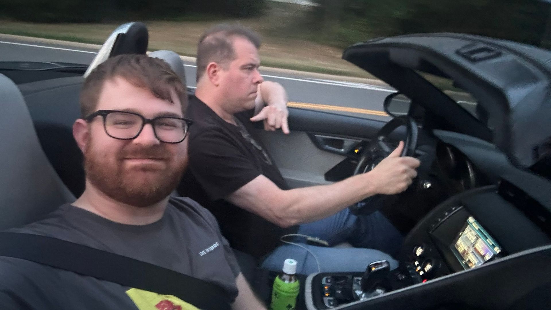A man with a beard and glasses sitting next to a man driving a car