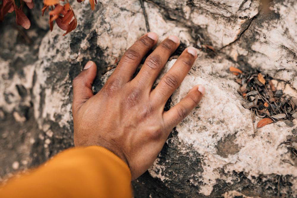 A man is pictured pressing his hand against a large stone
