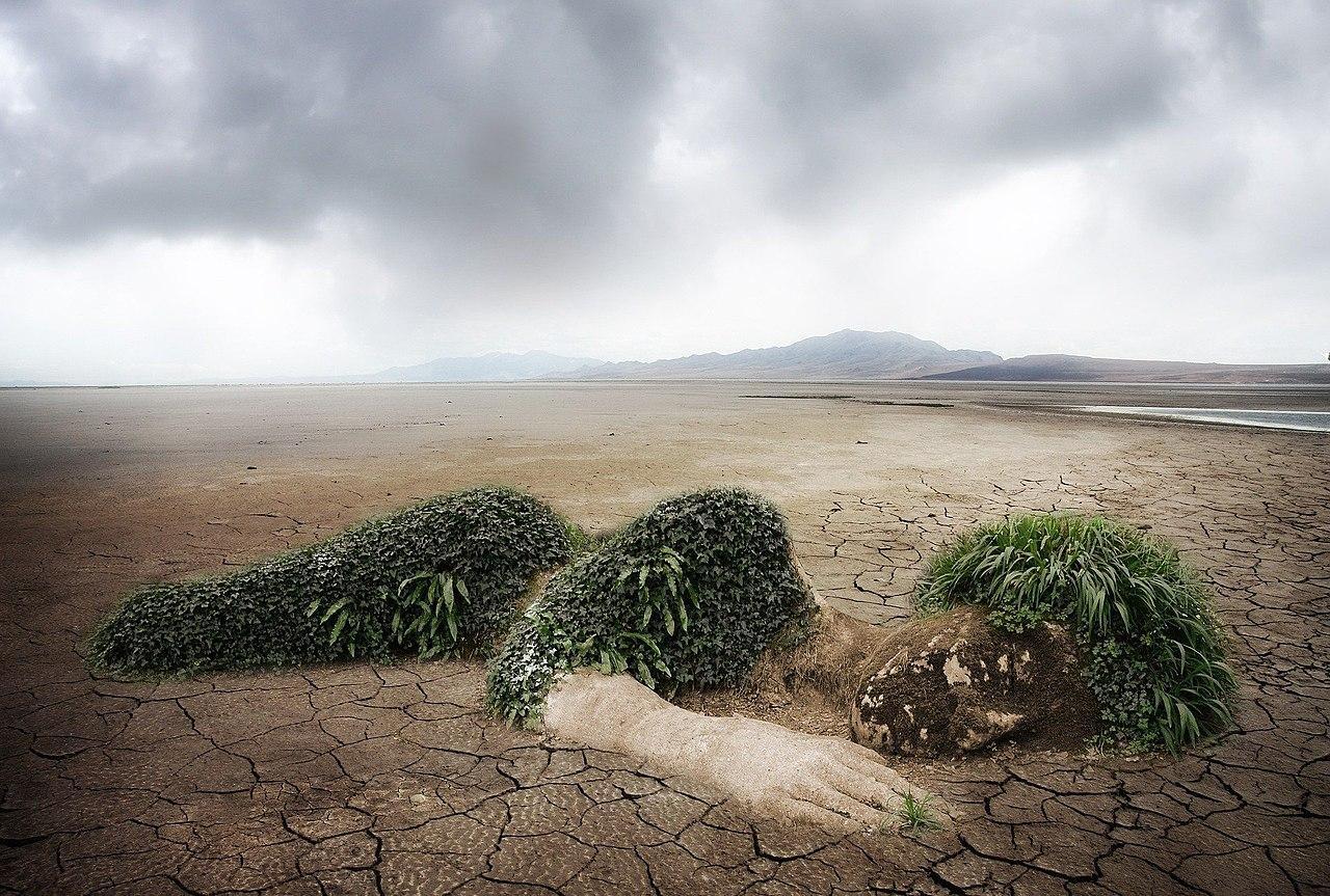 Dry, cracked ground with the earth shaped as a person laying down to personify climate change. Green leaves represent clothes and hair.