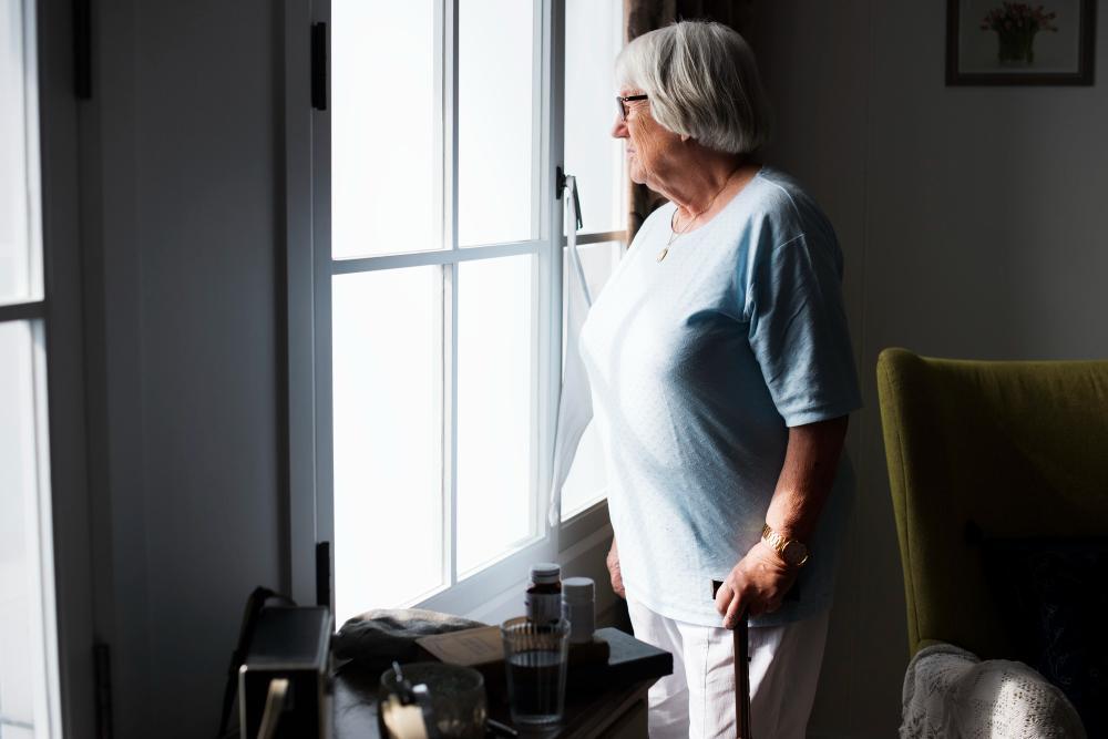 A photograph of an older woman staring out a window